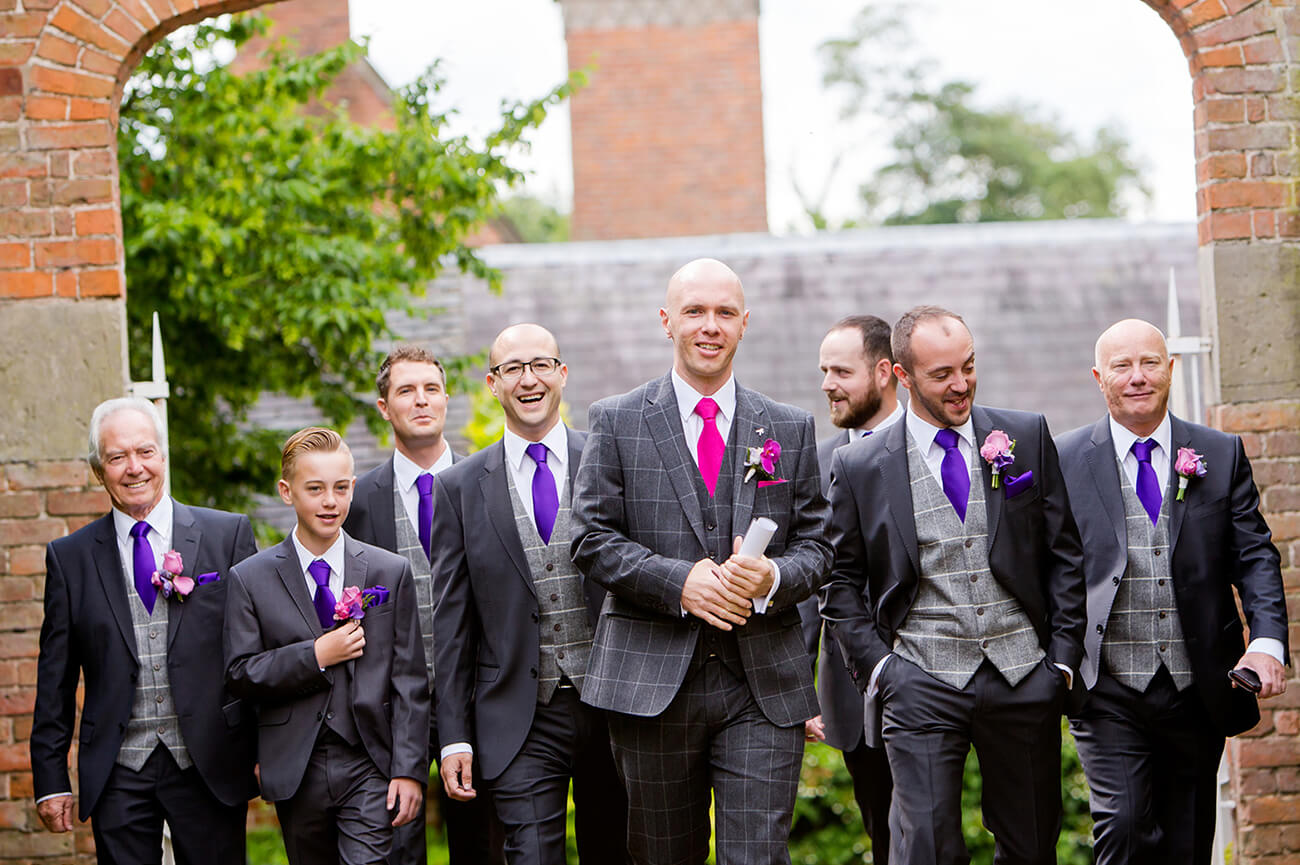 The groom and his groomsmen make their way to the wedding ceremony wearing matching suits and ties – purple wedding theme