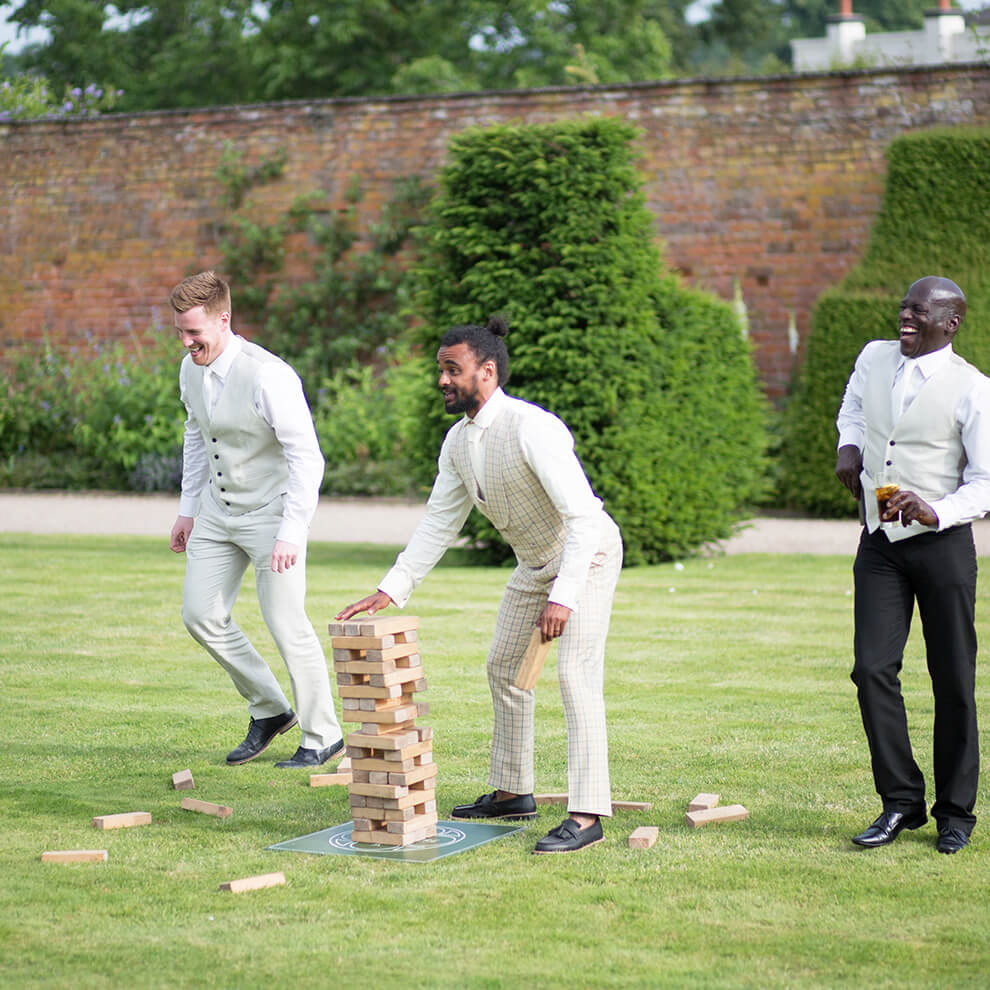 The groom enjoys a game of jenga on the lawns at Combermere Abbey wedding venue in Cheshire