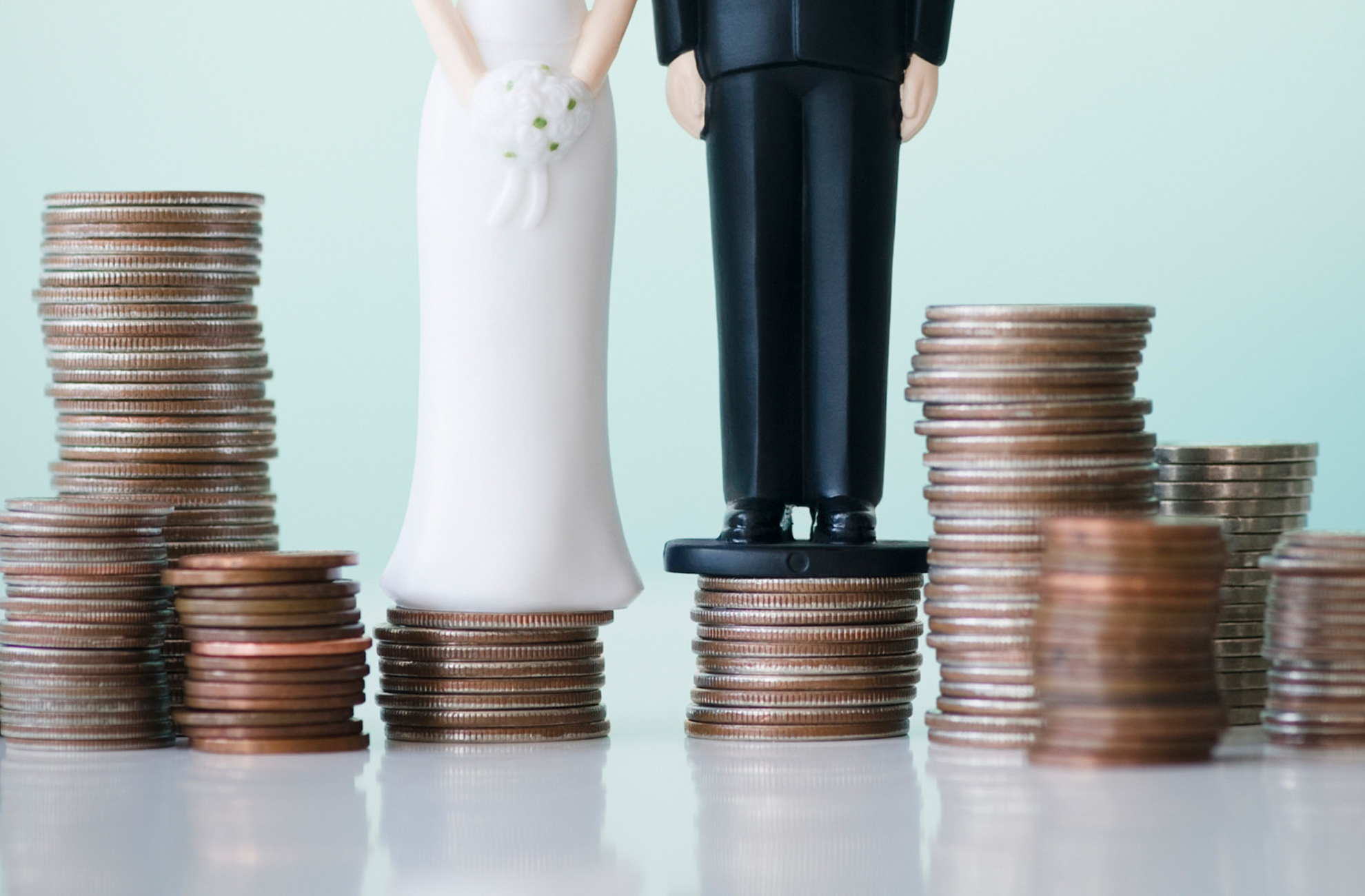 A bride and groom cake topper sit on top of coins – wedding budget